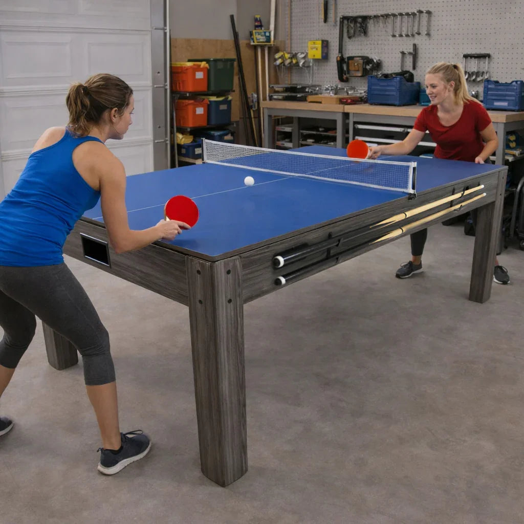 7-in-1 games table with a blue surface, sturdy grey wood frame, and two players enjoying a game of table tennis in a garage setting