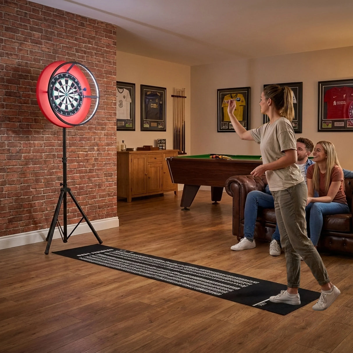 Dart board set with vibrant LED surround, mounted on a stand, with a player aiming while friends relax on a couch in a cozy game room