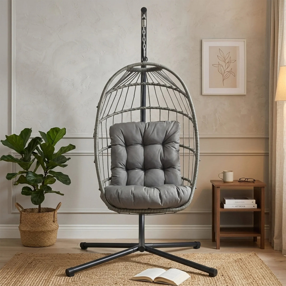 Grey rattan hanging egg chair with plush cushion, suspended from a sleek metal stand, set in a cozy, modern living room environment