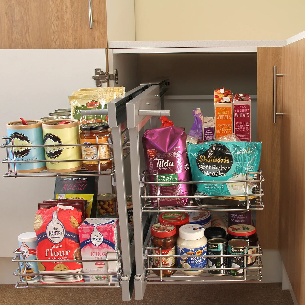 Right-hand pull-out kitchen cupboard drawers with silver metal frames, showcasing organized pantry items and jars in a wooden cabinet