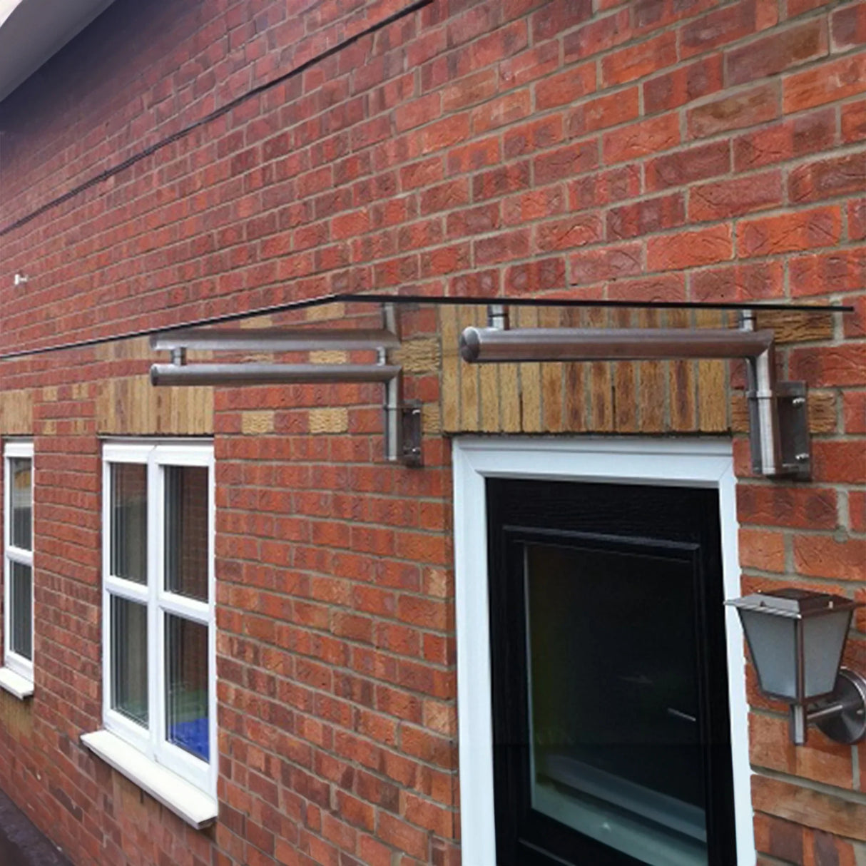 Glass door canopy with stainless steel brackets, 120cm wide by 80cm deep, mounted above a brick wall, enhancing entrance protection