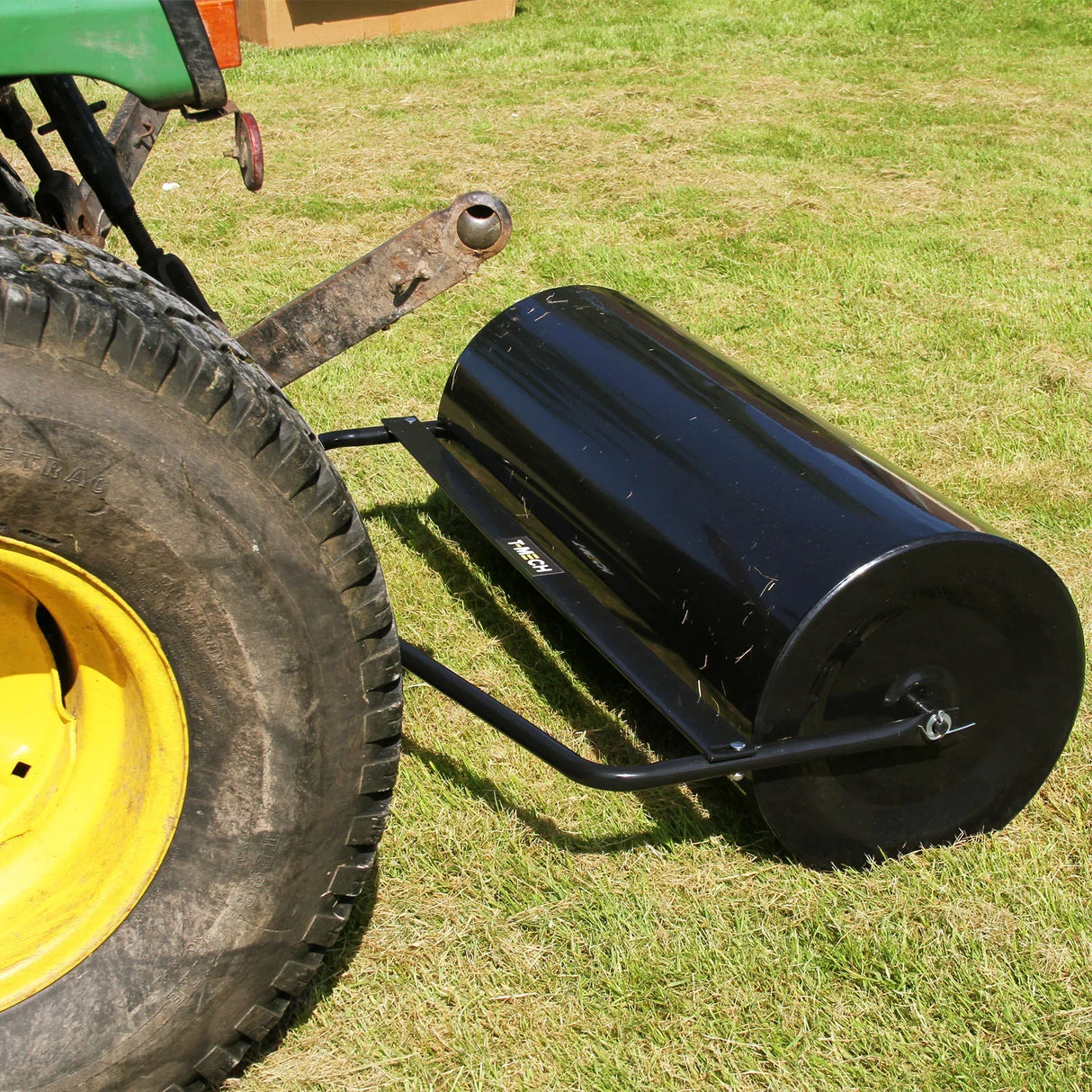 T-Mech 120L towable garden roller with a glossy black finish, attached to a tractor, resting on green grass for lawn leveling