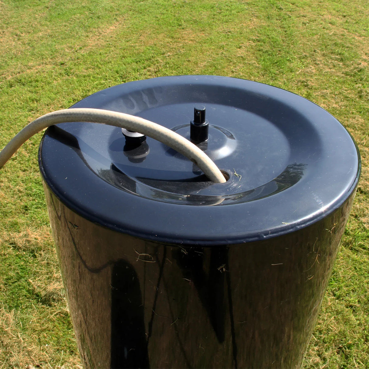 Black cylindrical top of the T-Mech 120L Towable Garden Roller with a hose connection, set against a grassy background