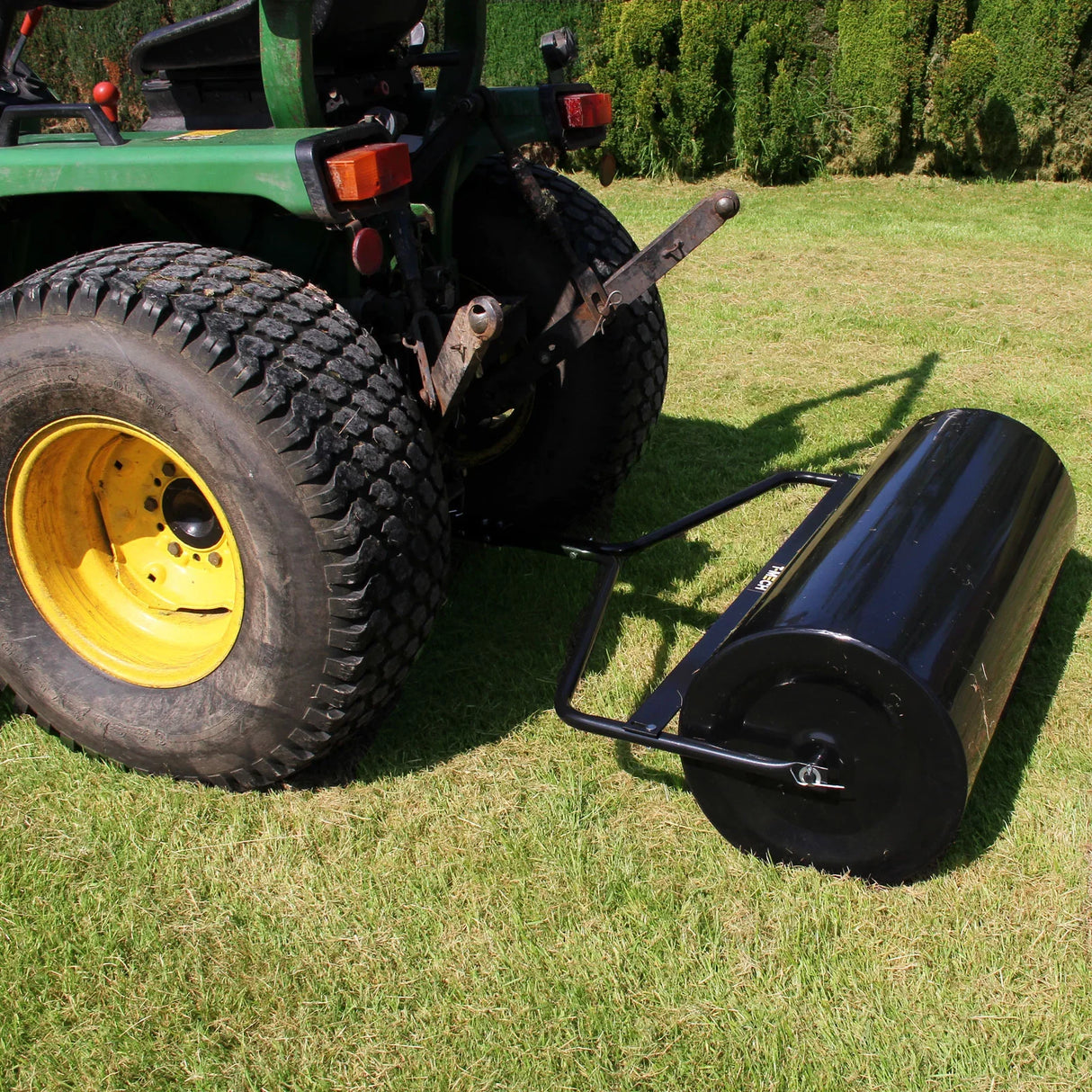 T-Mech 120L Towable Garden Roller in black, attached to a tractor, resting on green grass with textured tires visible