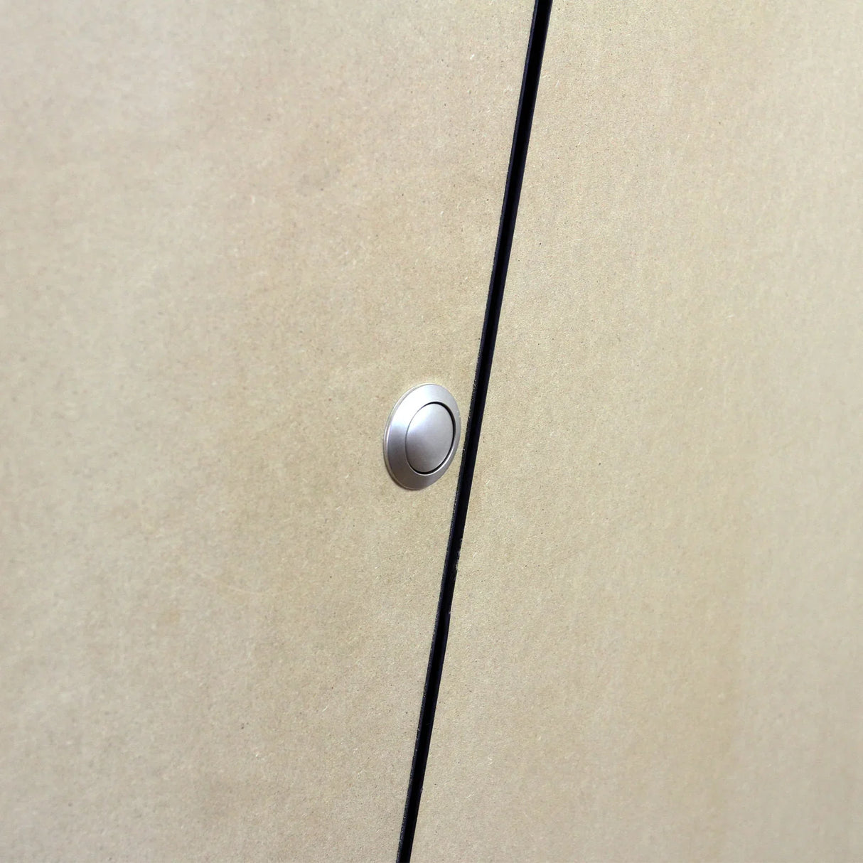 Close-up of a sleek, silver push button on a smooth, light brown MDF surface of a camper van kitchen unit
