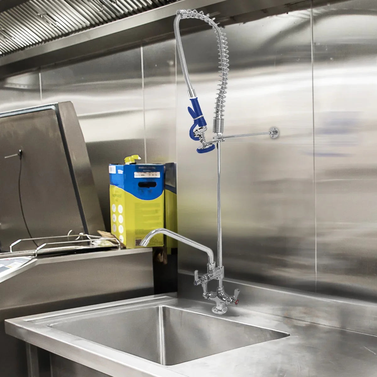 Stainless steel KuKoo pre-rinse commercial tap with flexible hose and blue handle, mounted above a stainless steel sink in a kitchen setting