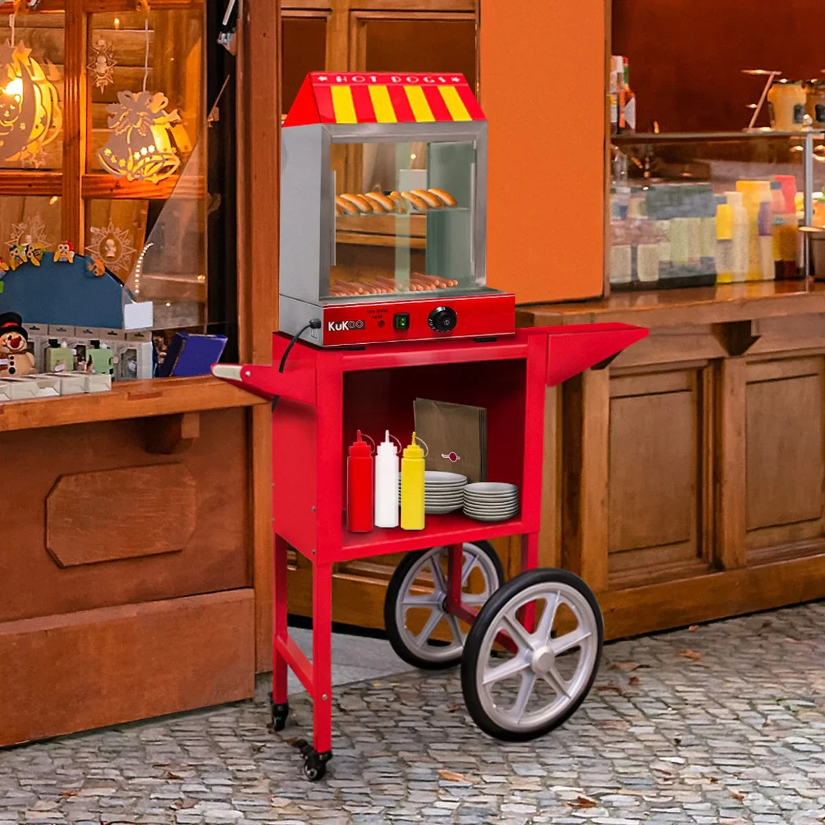 Bright red KuKoo hot dog steamer cart with a glass top, wheels, and condiment holders, perfect for outdoor events and food stalls