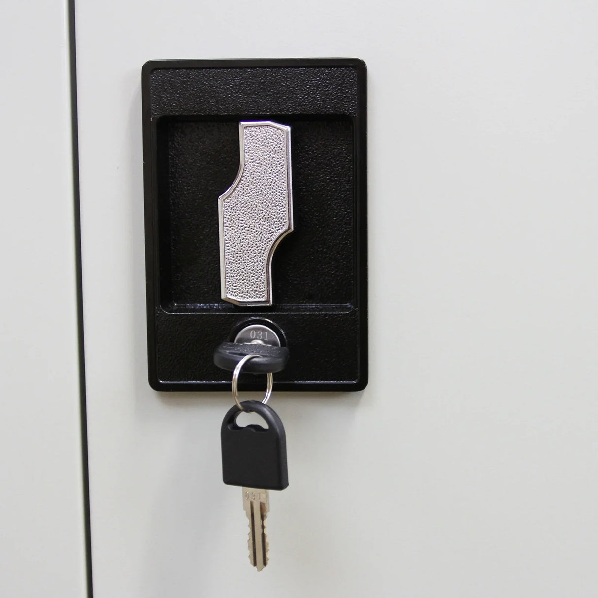Close-up of a silver key inserted in a textured black lock on a light gray metal filing cabinet, showcasing security features