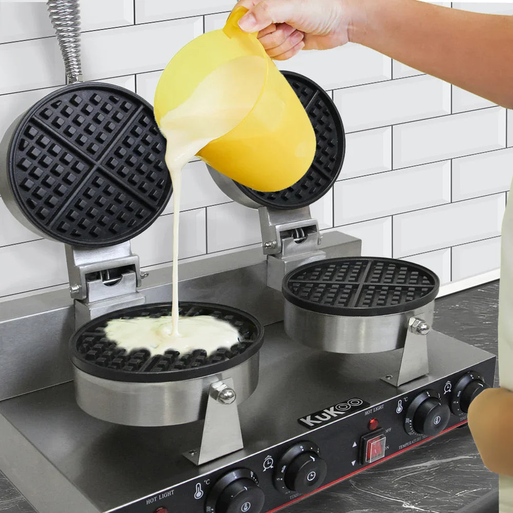 KuKoo Double Waffle Maker with two round, non-stick waffle plates, pouring batter from a yellow jug, stainless steel base, and control knobs