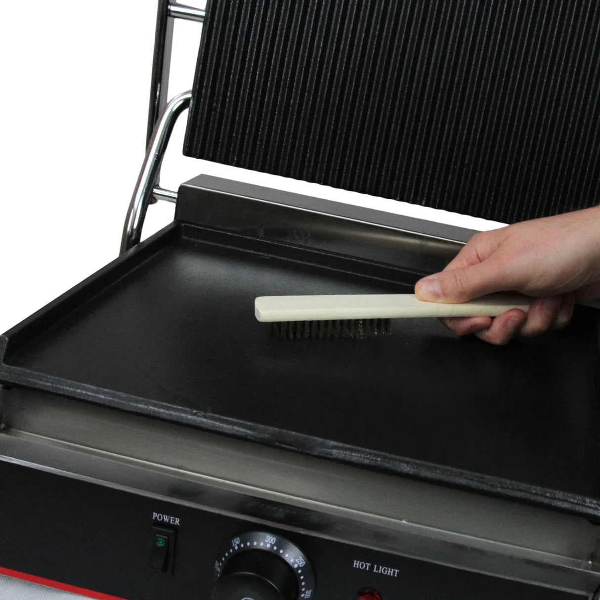 Grooved and flat cooking surface of the KuKoo Panini Press with a hand holding a brush for cleaning, featuring a sleek design