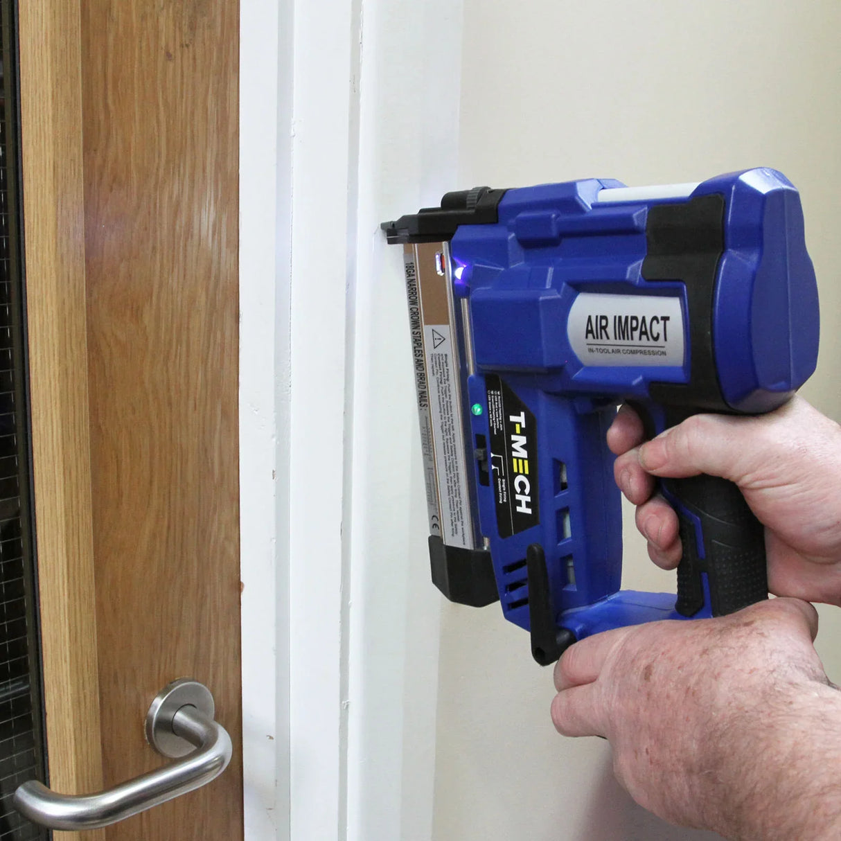 T-Mech Nail & Staple Gun in blue, featuring a textured grip, positioned against a white wall, demonstrating its air impact functionality