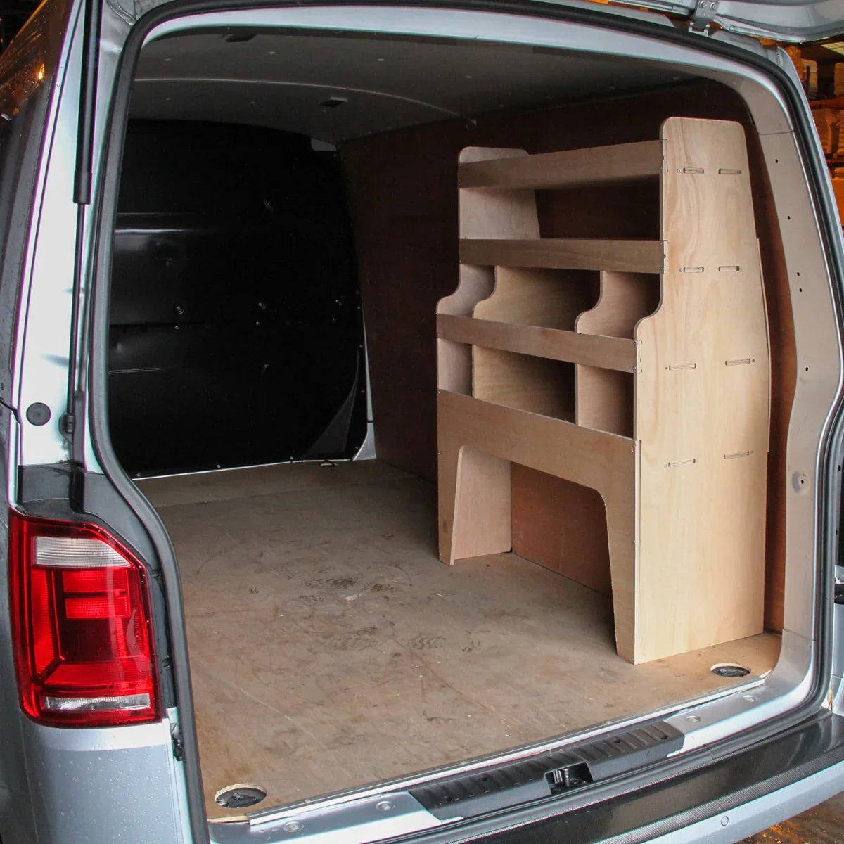 Black van interior featuring a wooden racking unit with three shelves, designed for VW Transporter, on a plywood floor