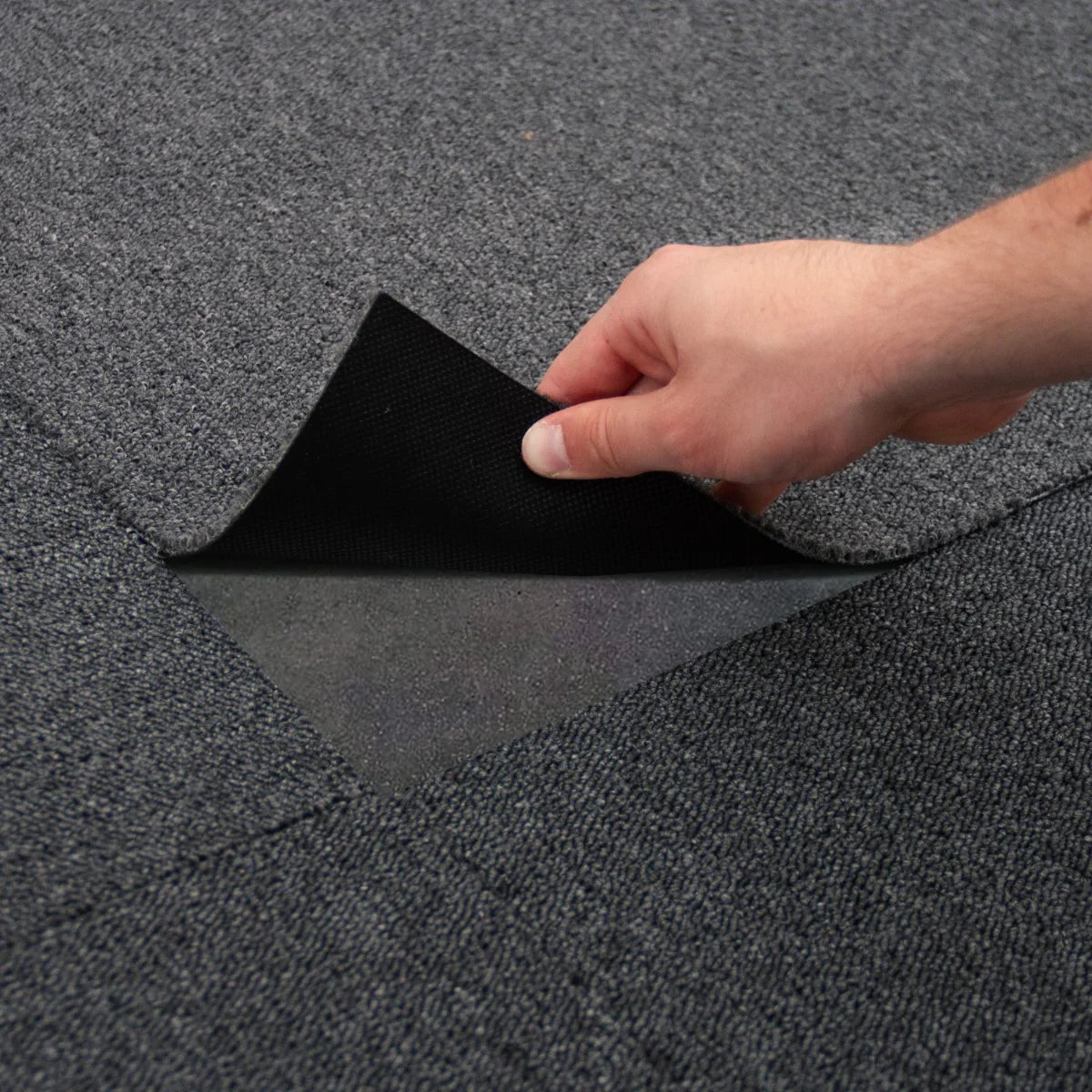 Charcoal black carpet tile being lifted to show its textured surface and backing, ideal for versatile flooring solutions