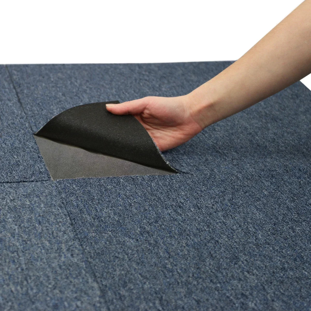 Storm blue carpet tile being lifted, showcasing its textured surface and sturdy backing, ideal for versatile flooring solutions