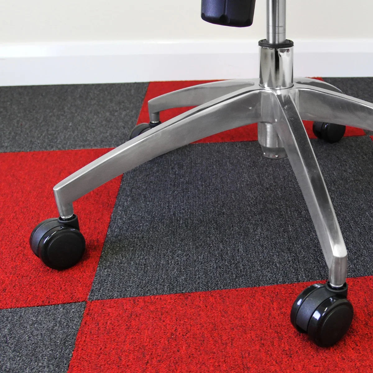 Scarlet red and charcoal gray carpet tiles arranged in a checkerboard pattern, with a sleek office chair on rolling wheels