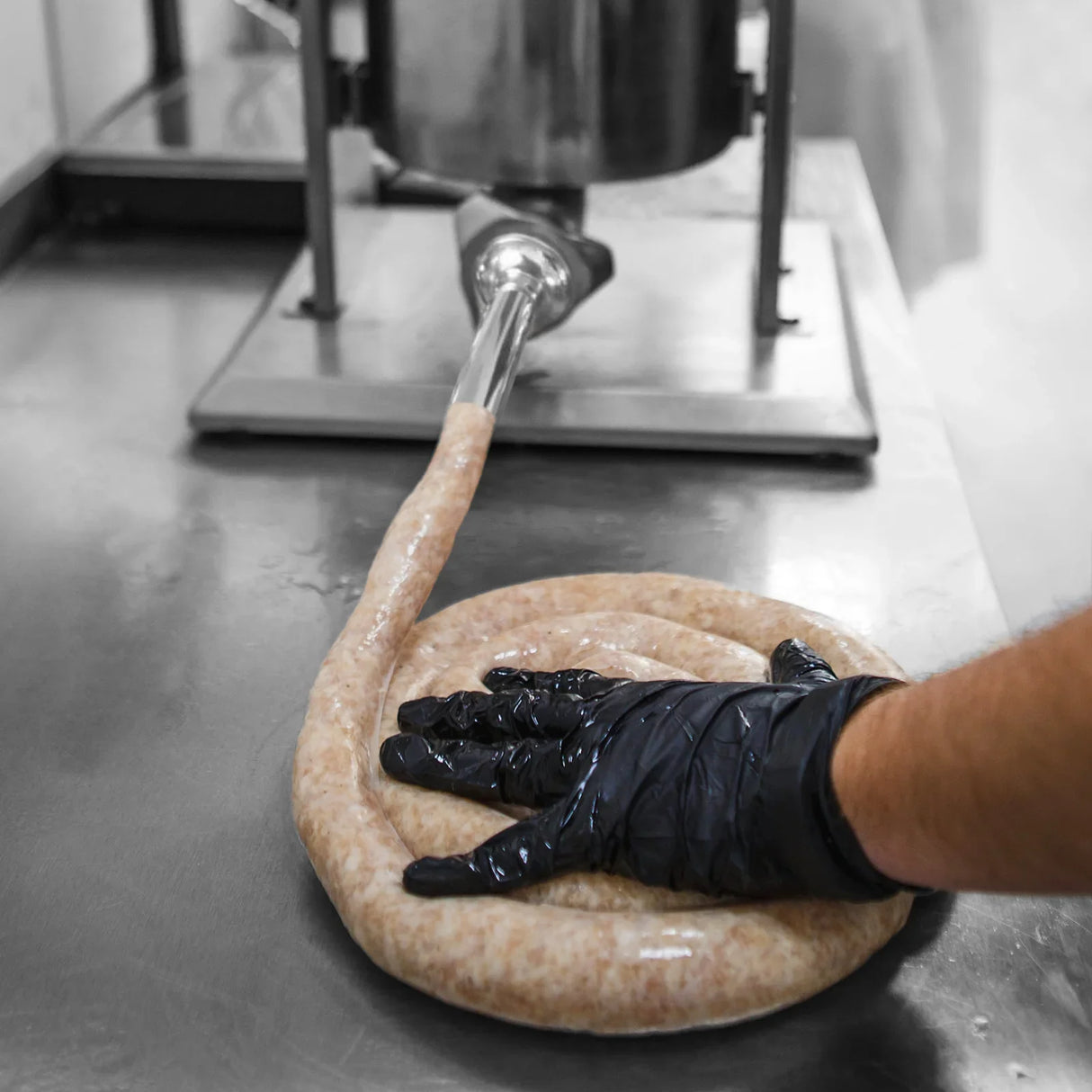 KuKoo 3L sausage stuffer in use, with a gloved hand shaping fresh sausage links on a stainless steel countertop