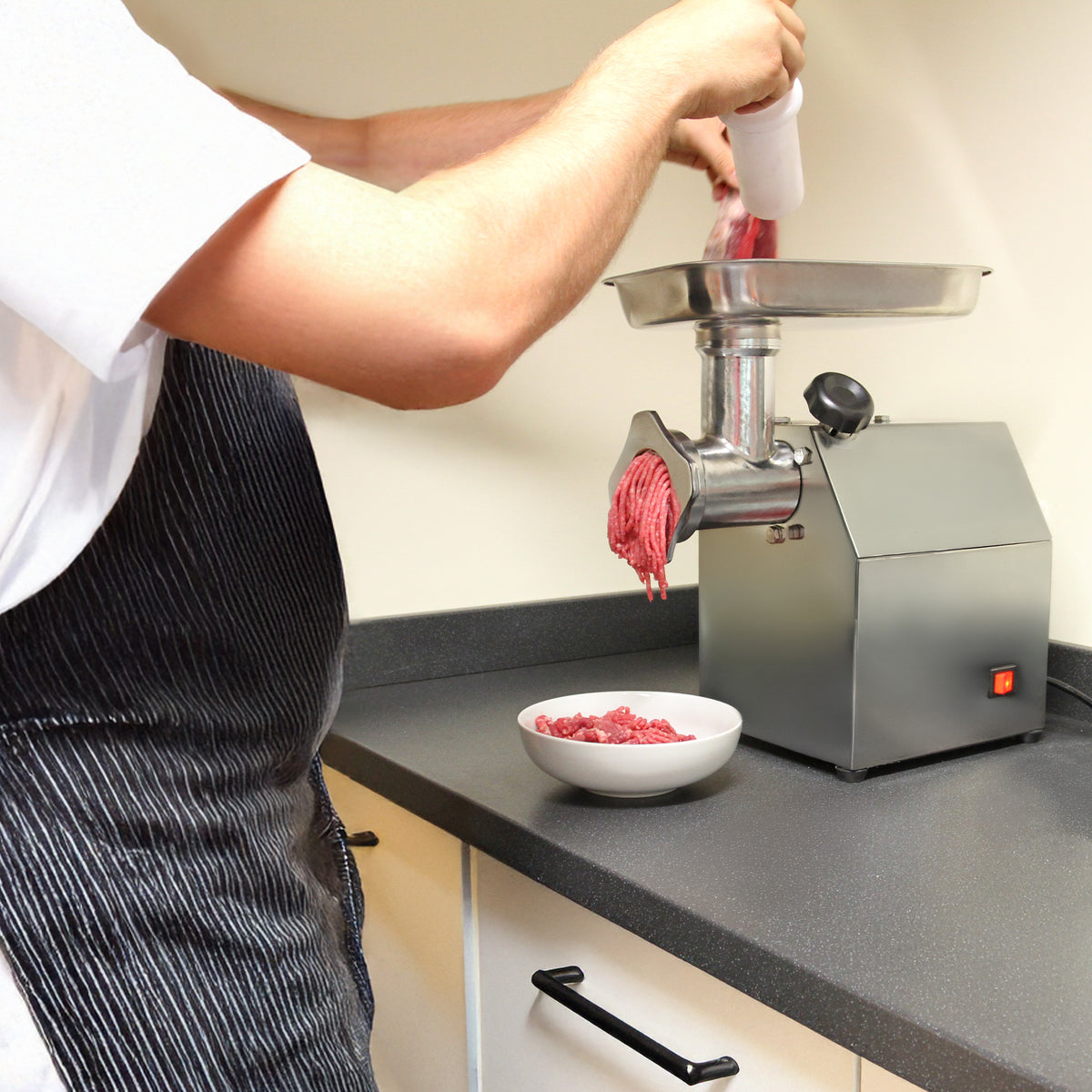 Stainless steel KuKoo commercial meat grinder with ground beef being processed into a white bowl on a black countertop