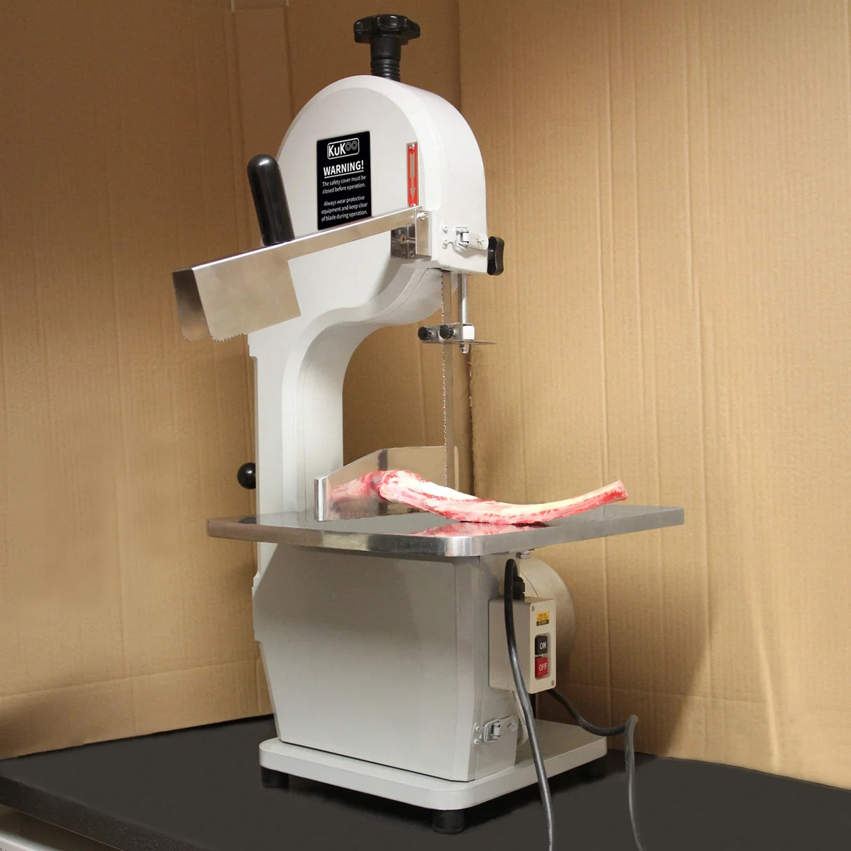 Kukoo Commercial Bone Saw Bandsaw with a white body, stainless steel cutting area, and a bone resting on the cutting table