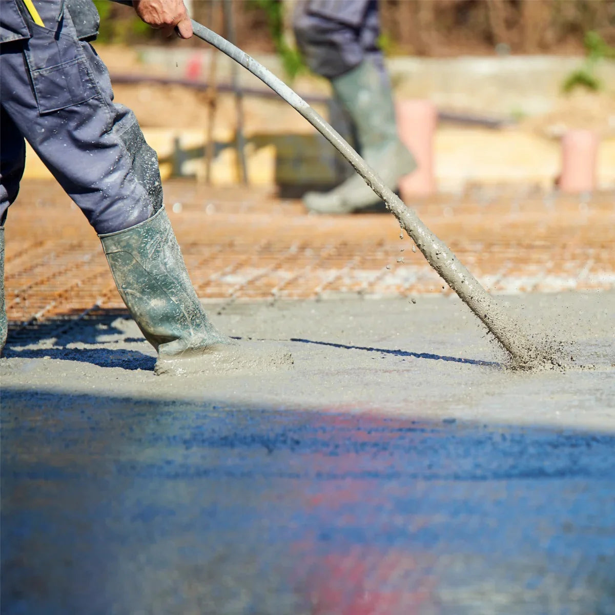 Cement mixer and handheld concrete vibrator in action, pouring wet concrete with a 2m shaft, worker in rubber boots on site