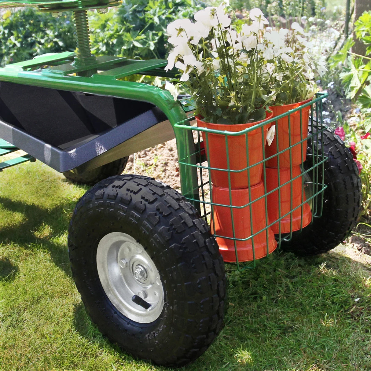 Heavy-duty mobile garden seat with green frame, large black tires, and a wire basket holding orange gardening boots and white flowers