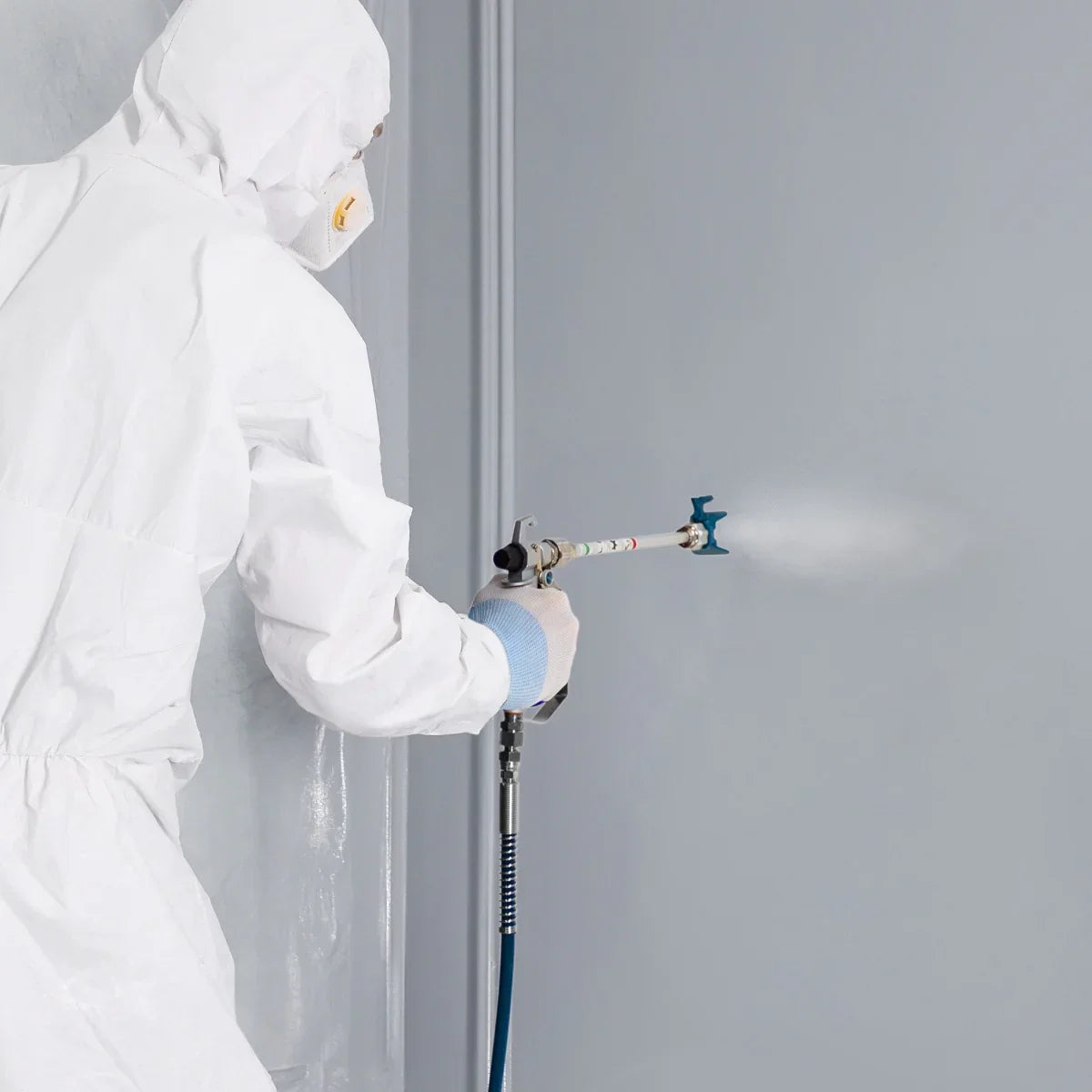 Maxblast Airless Paint Sprayer Gun in use, featuring a sleek design, white protective suit, and fine mist spraying on a gray wall
