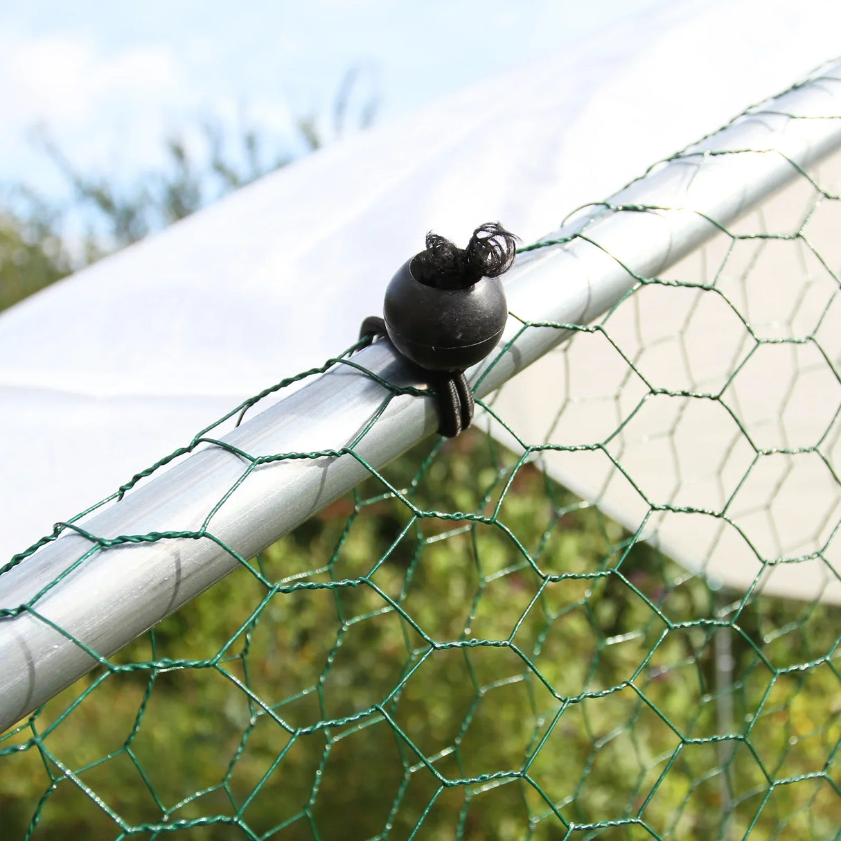 Close-up of a green chicken run netting secured with a black clip on a silver metal frame, showcasing durable construction and secure fastening