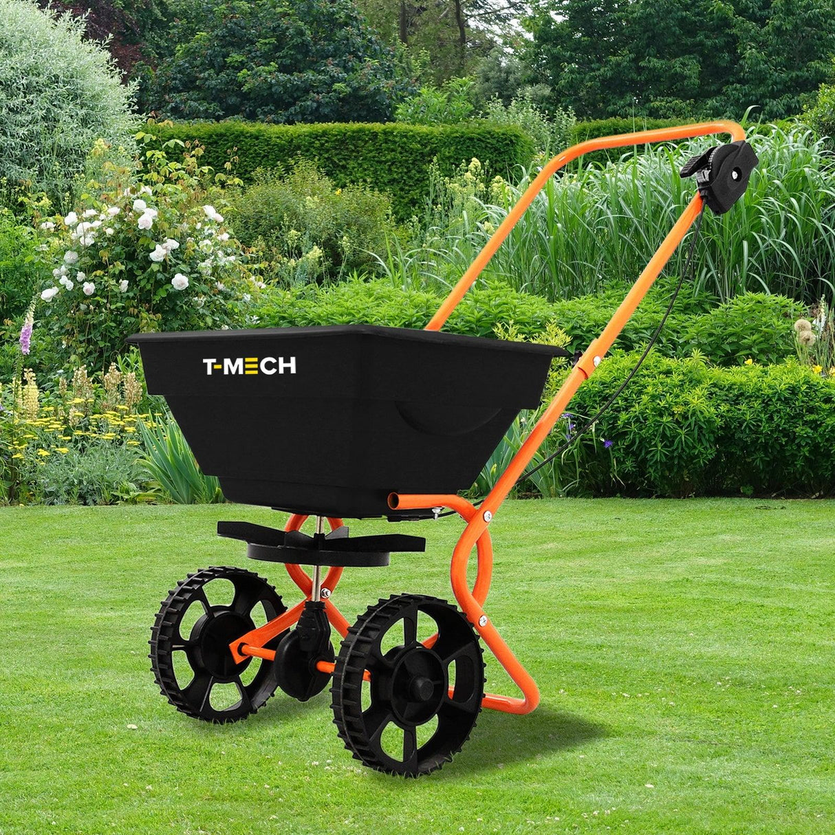 T-Mech Rotary Spreader with a black hopper, orange frame, and sturdy wheels, set against a lush green garden backdrop