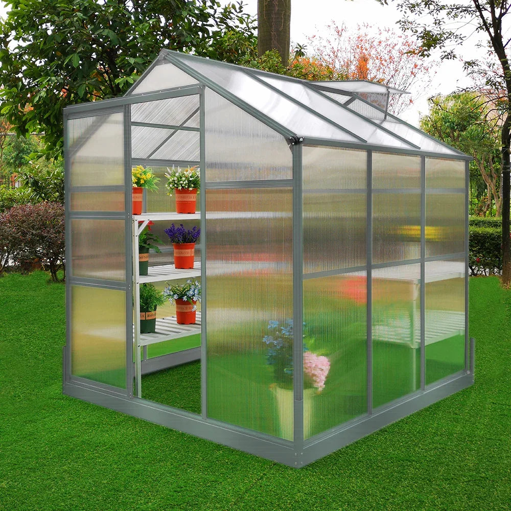 Greenhouse 6ft x 6ft with a sturdy base, featuring two water-resistant racks and vibrant potted plants inside, set on green grass