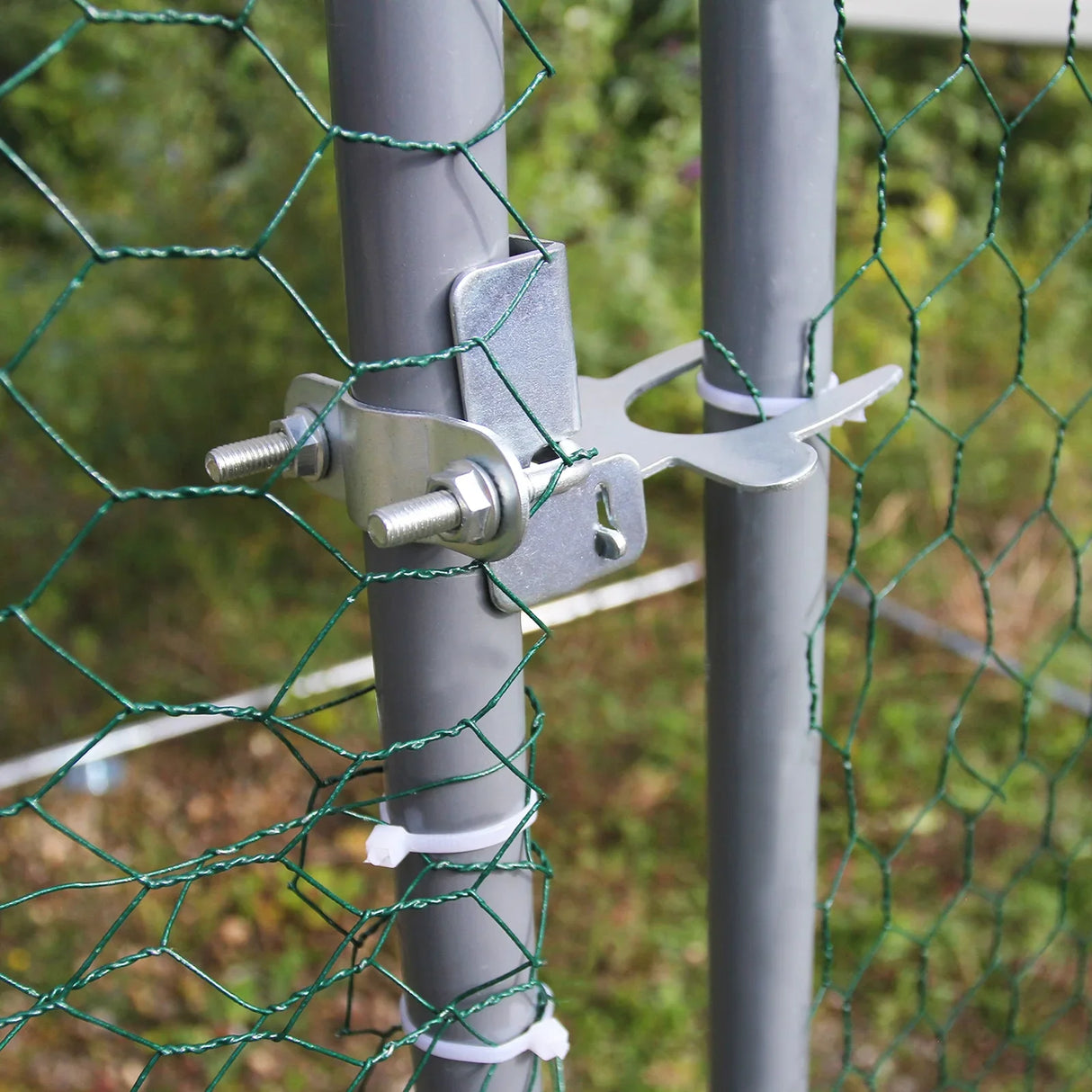 Close-up of a metal latch securing green chicken wire to a gray post, showcasing durability and easy access for the Chicken Run enclosure