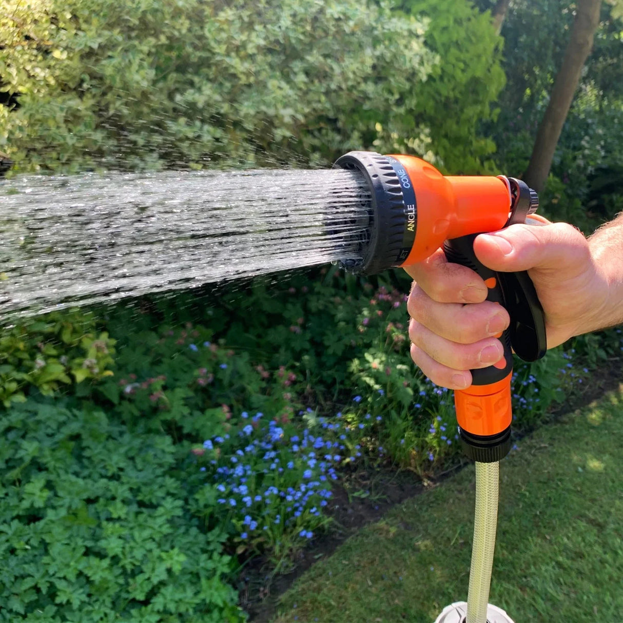 Retractable 20m hosepipe with an orange spray nozzle, water flowing from the nozzle, set against a lush garden backdrop