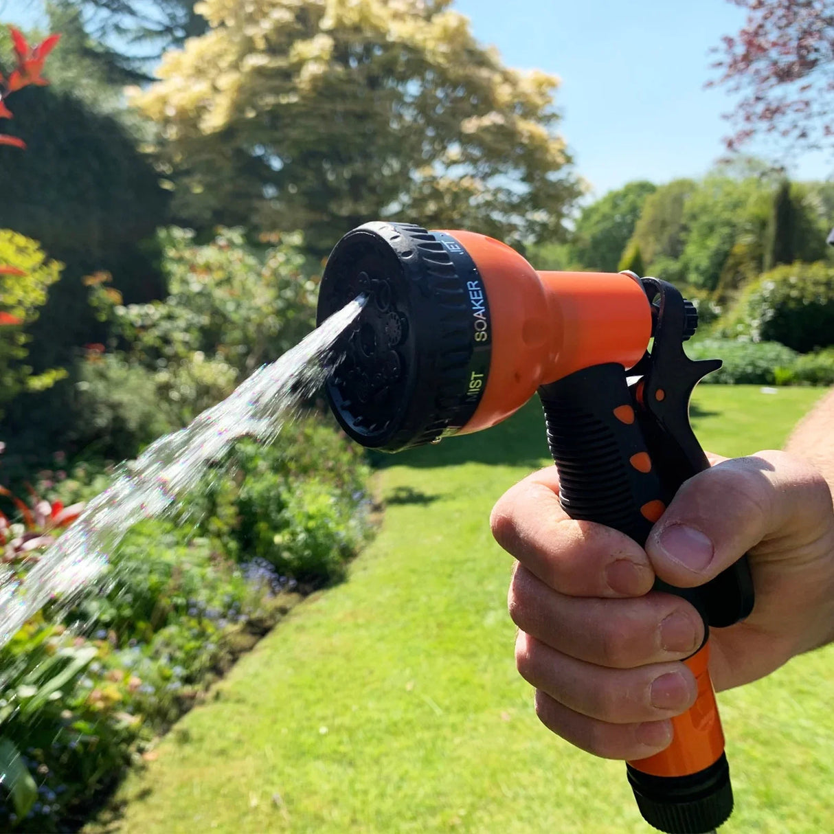 Retractable 20m hosepipe with a vibrant orange spray nozzle, showcasing a hand holding it, spraying water in a lush garden setting