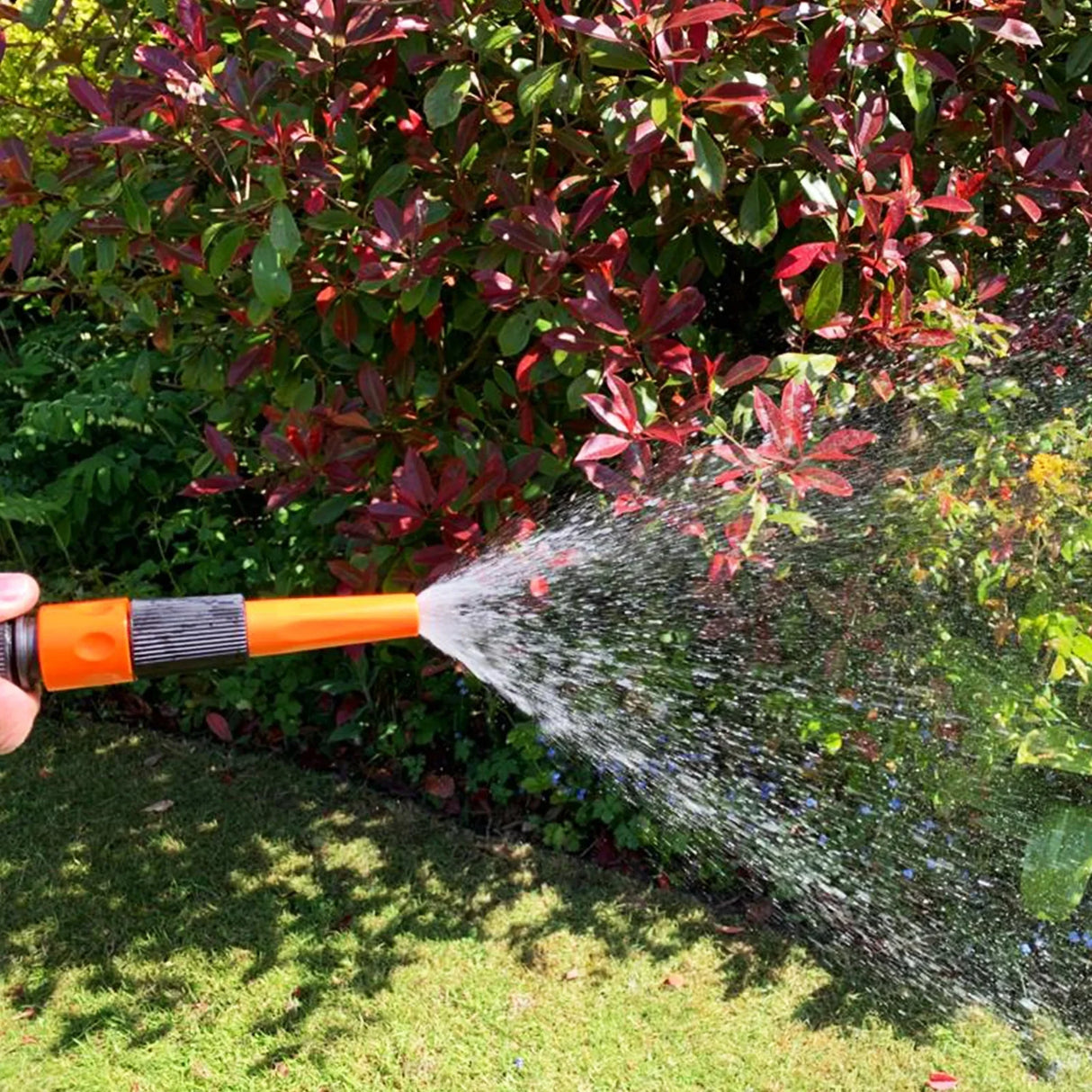 Retractable 20m hosepipe with a vibrant orange nozzle spraying water, surrounded by lush green grass and colorful foliage