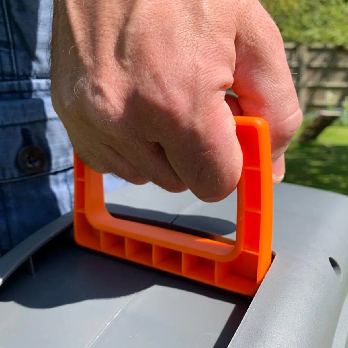 Close-up of a hand gripping the bright orange handle of a 30m retractable hosepipe, showcasing its ergonomic design and sturdy construction