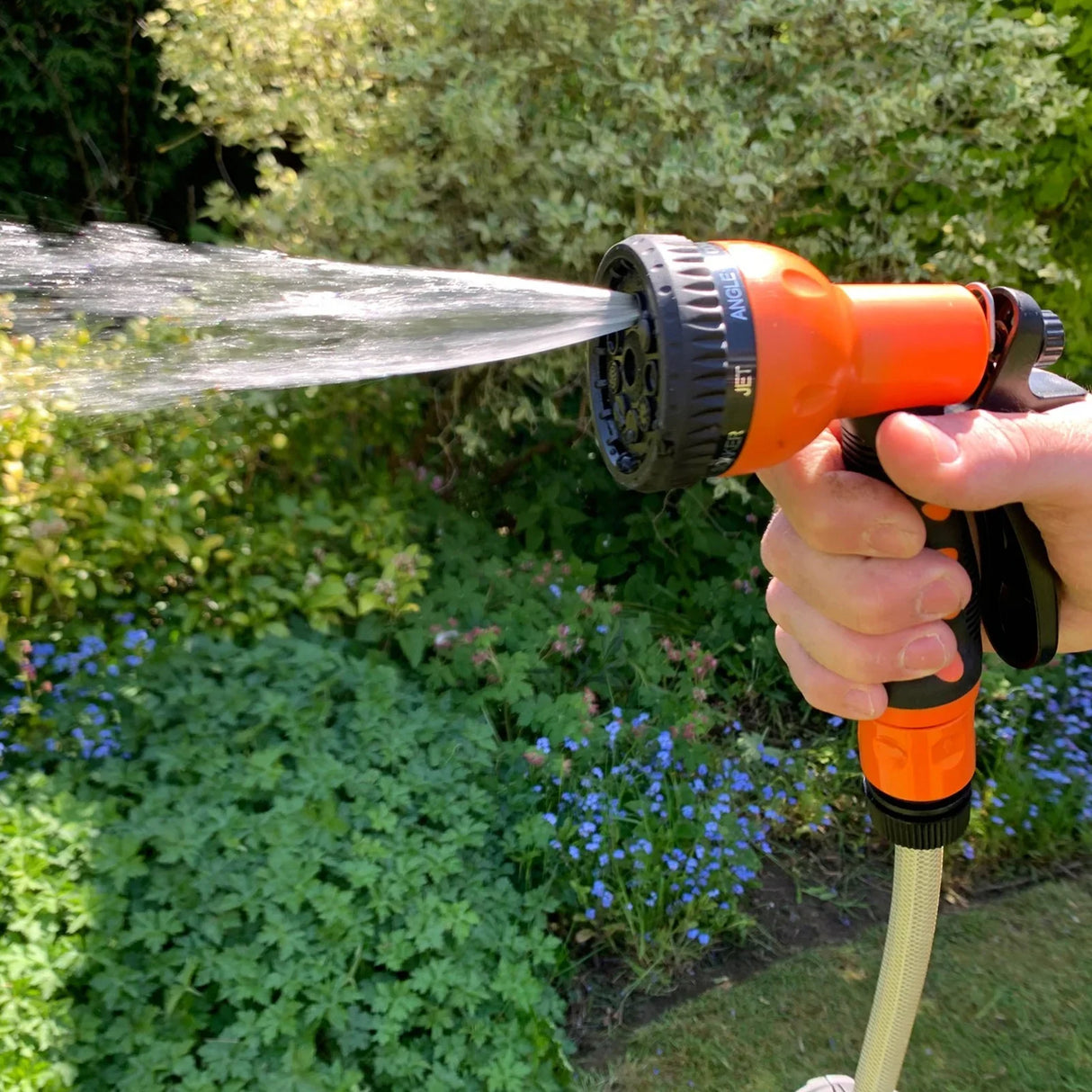 Retractable 30m hosepipe with an orange spray nozzle, demonstrating a powerful water jet against a lush garden backdrop