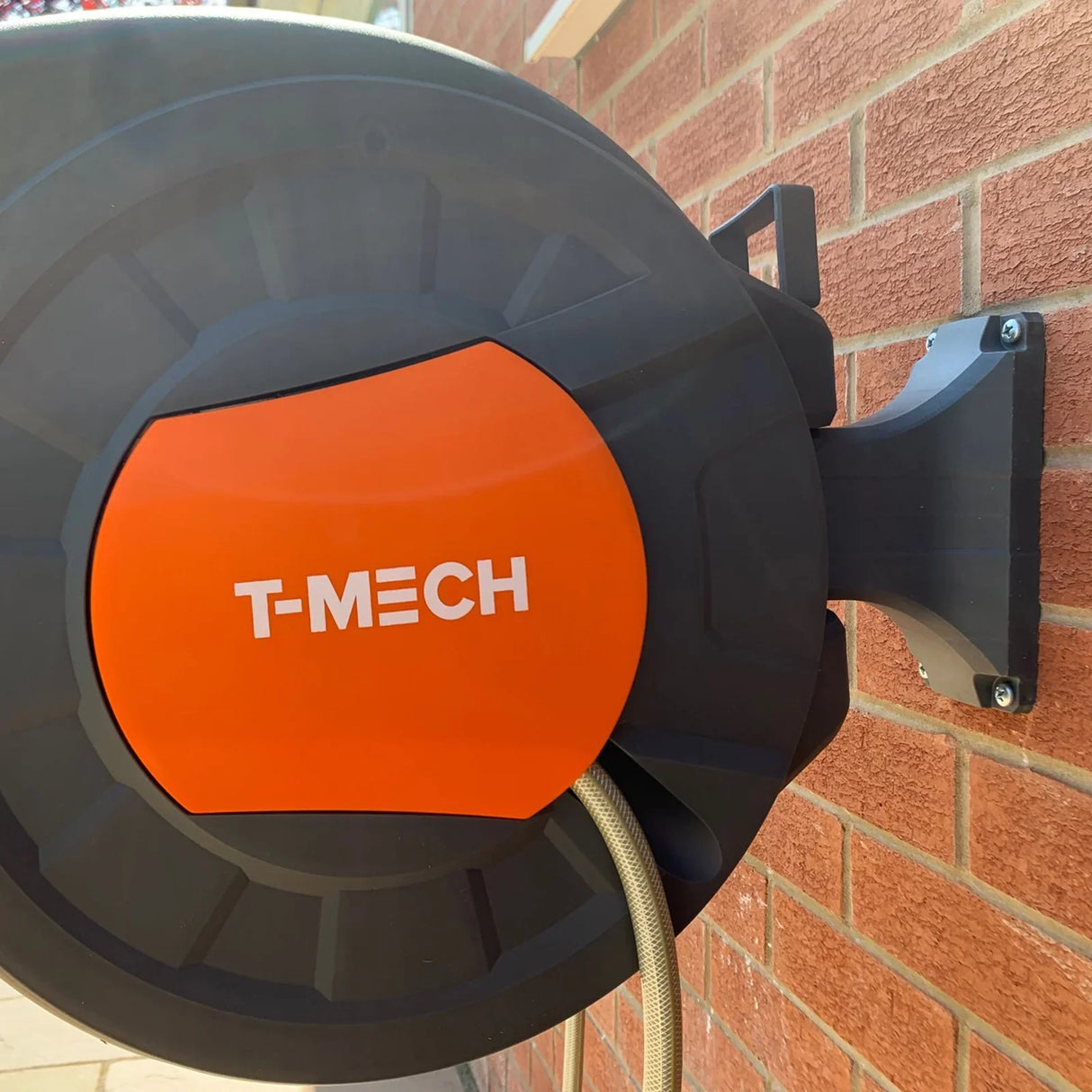 30m retractable hosepipe mounted on a brick wall, featuring a durable black casing with an orange front panel and the T-MECH logo