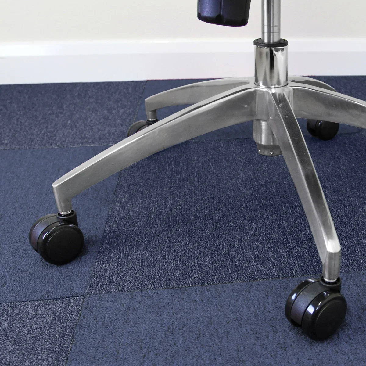 Storm blue carpet tiles arranged on a floor, showcasing a textured surface, with a sleek office chair on rolling casters above them