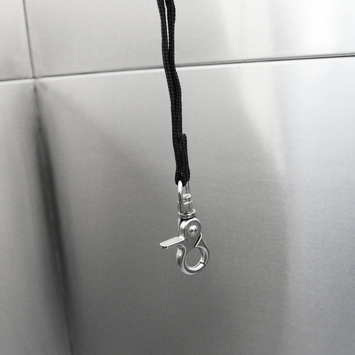 Stainless steel clip attached to a black cord, designed for securing pets during grooming in a wash station setup