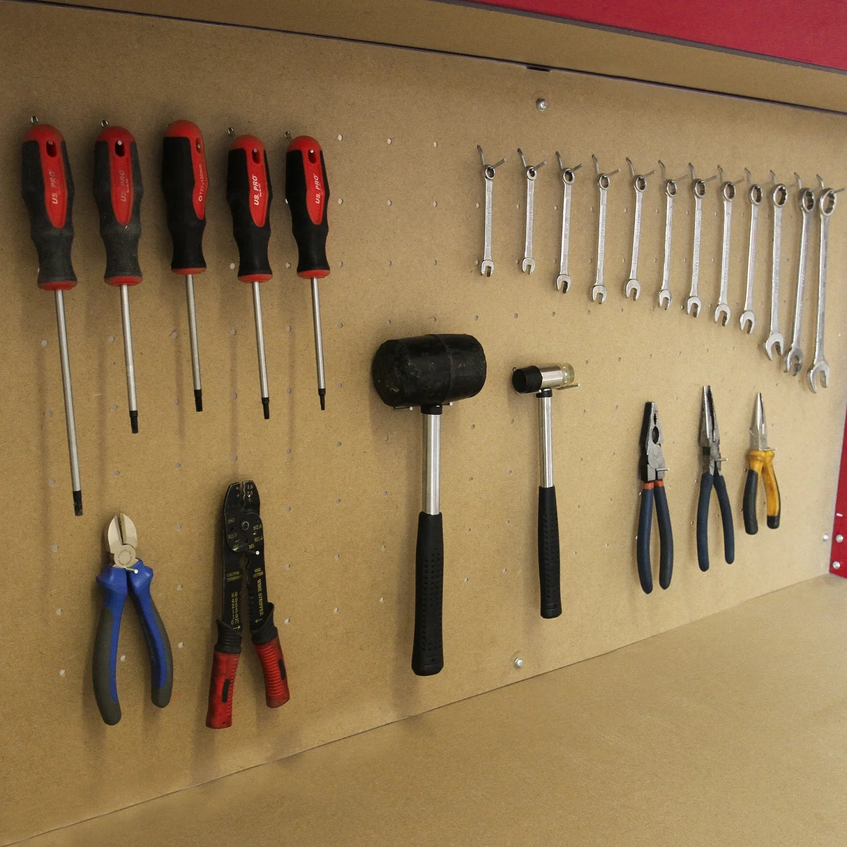 Red workbench featuring a pegboard with various hand tools including screwdrivers, wrenches, and pliers for organized storage