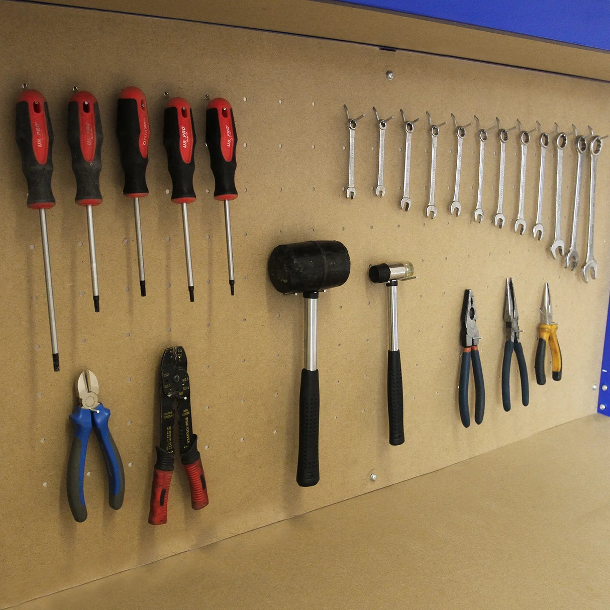 Blue workbench featuring a pegboard with various hand tools including screwdrivers, pliers, and wrenches neatly organized