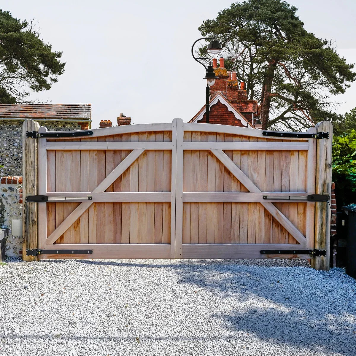 Electric swing gate opener set installed on a rustic wooden gate with a natural wood finish, framed by a gravel driveway and greenery