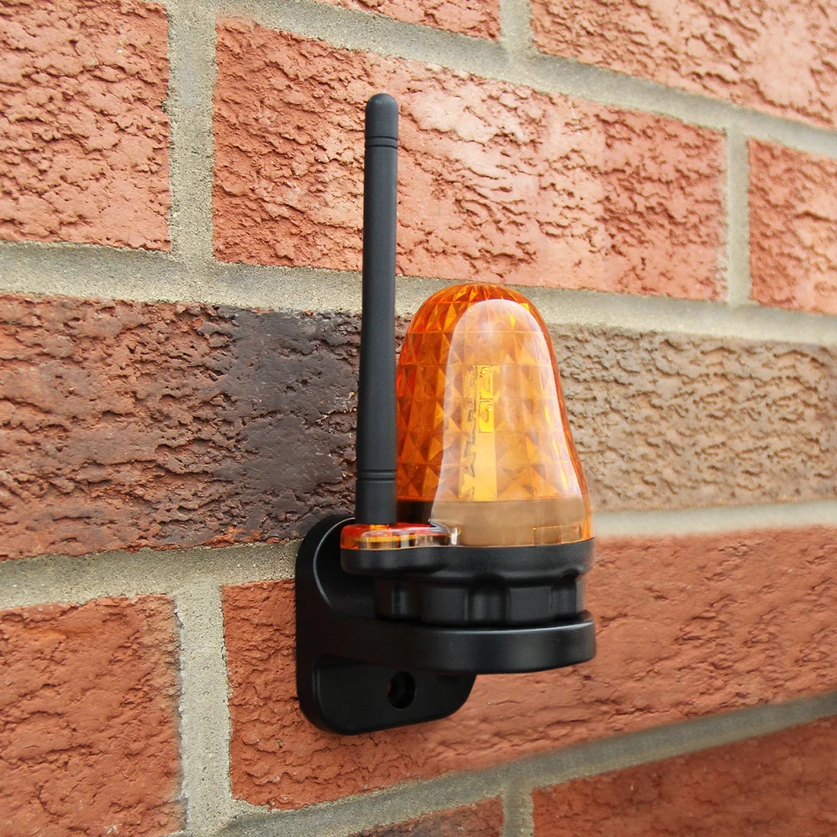 Amber warning light mounted on a textured brick wall, featuring a sleek design and a black base for the electric swing gate opener set