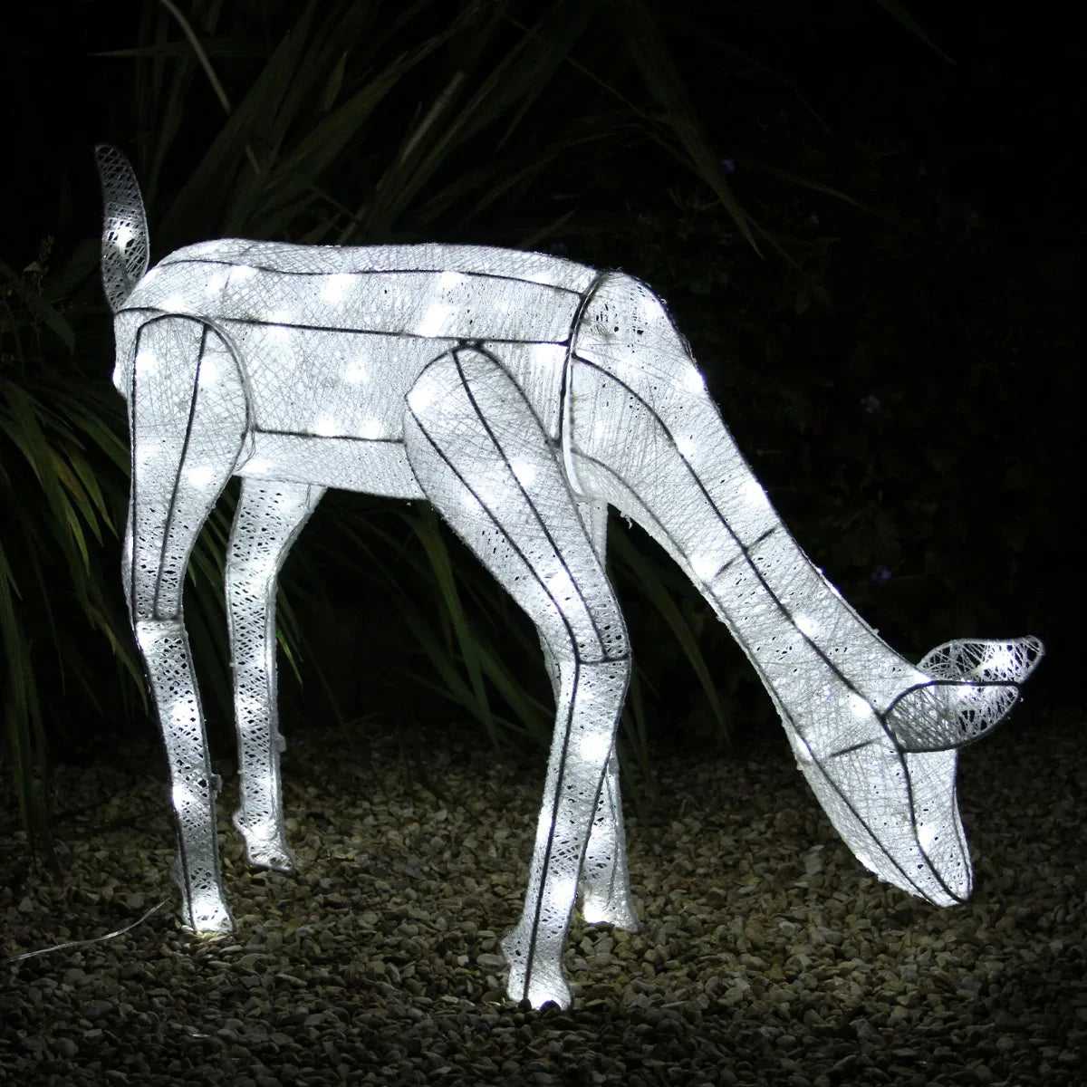 Glowing white doe sculpture with intricate cutout patterns, illuminated by warm LED lights, set against a dark garden backdrop