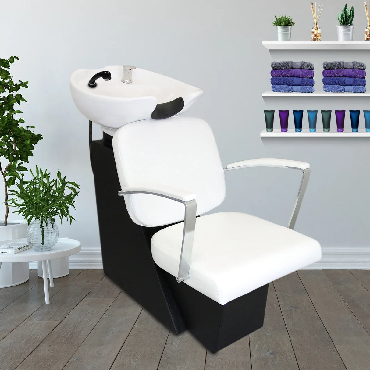 Sleek white salon backwash chair with chrome arms, featuring a built-in sink, set against a modern salon backdrop with towels and decor