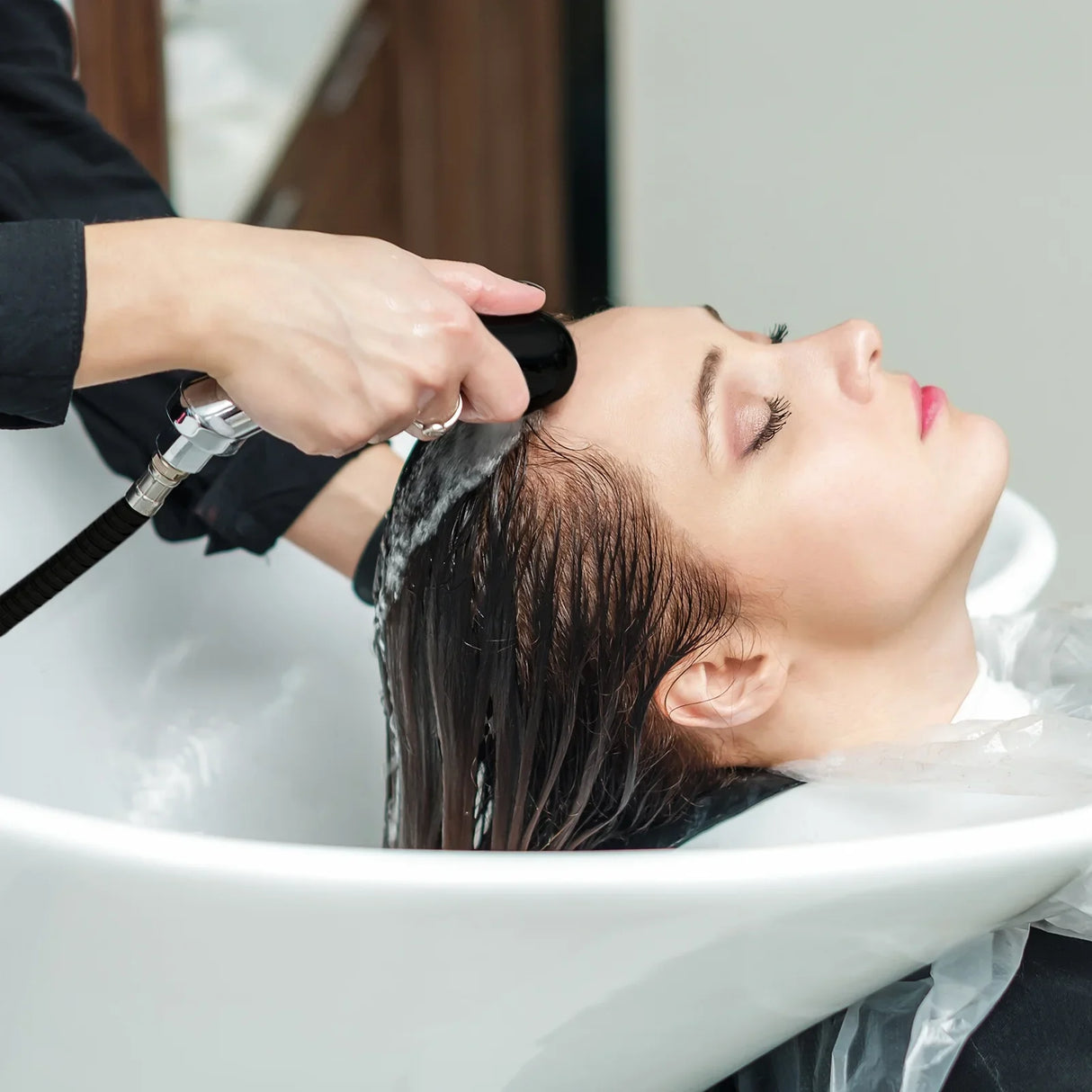 Black salon backwash chair with a client receiving a hair wash, featuring sleek design and comfortable headrest for relaxation