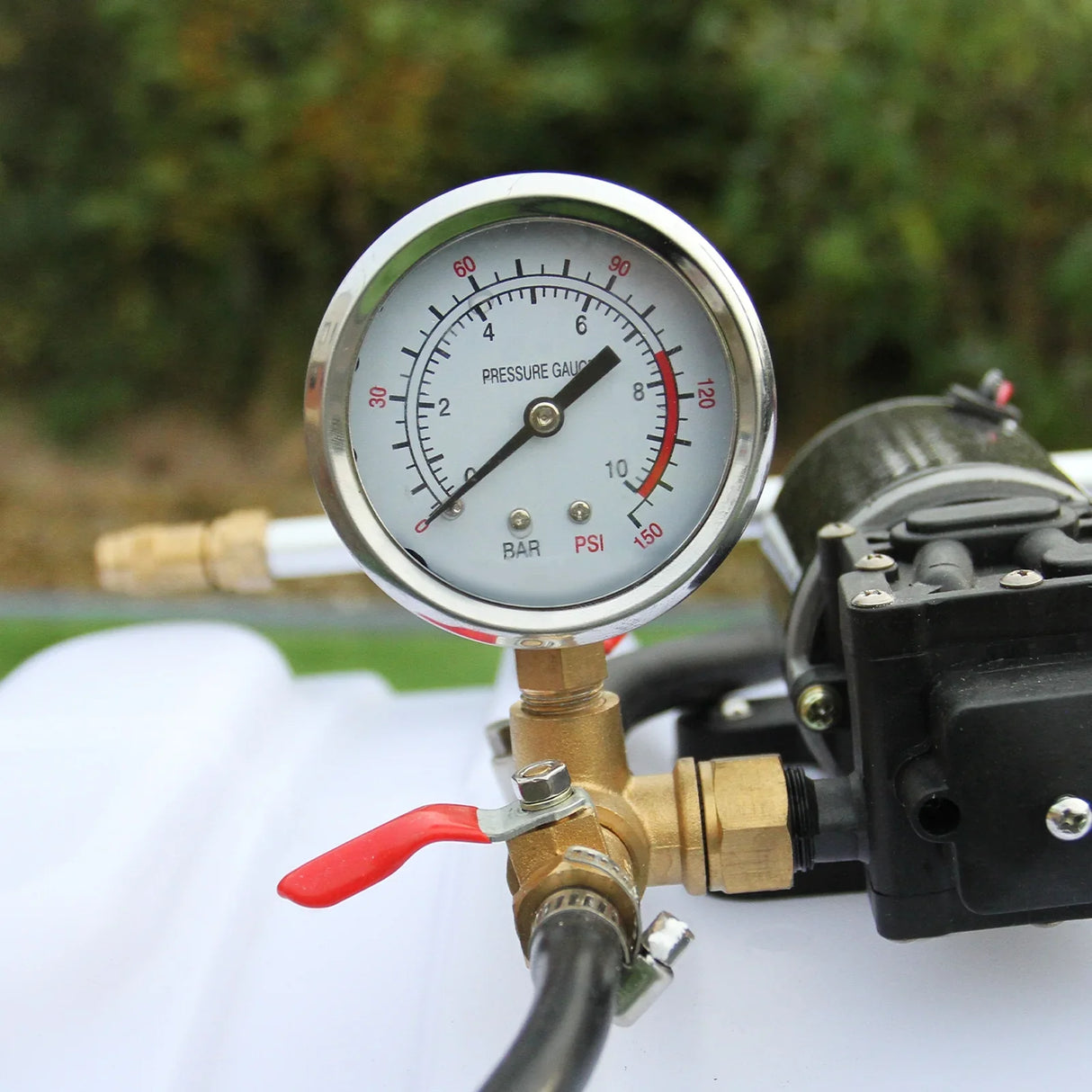 Pressure gauge on 100L ATV trailer sprayer, showing PSI and BAR readings, with brass fittings and red release valve