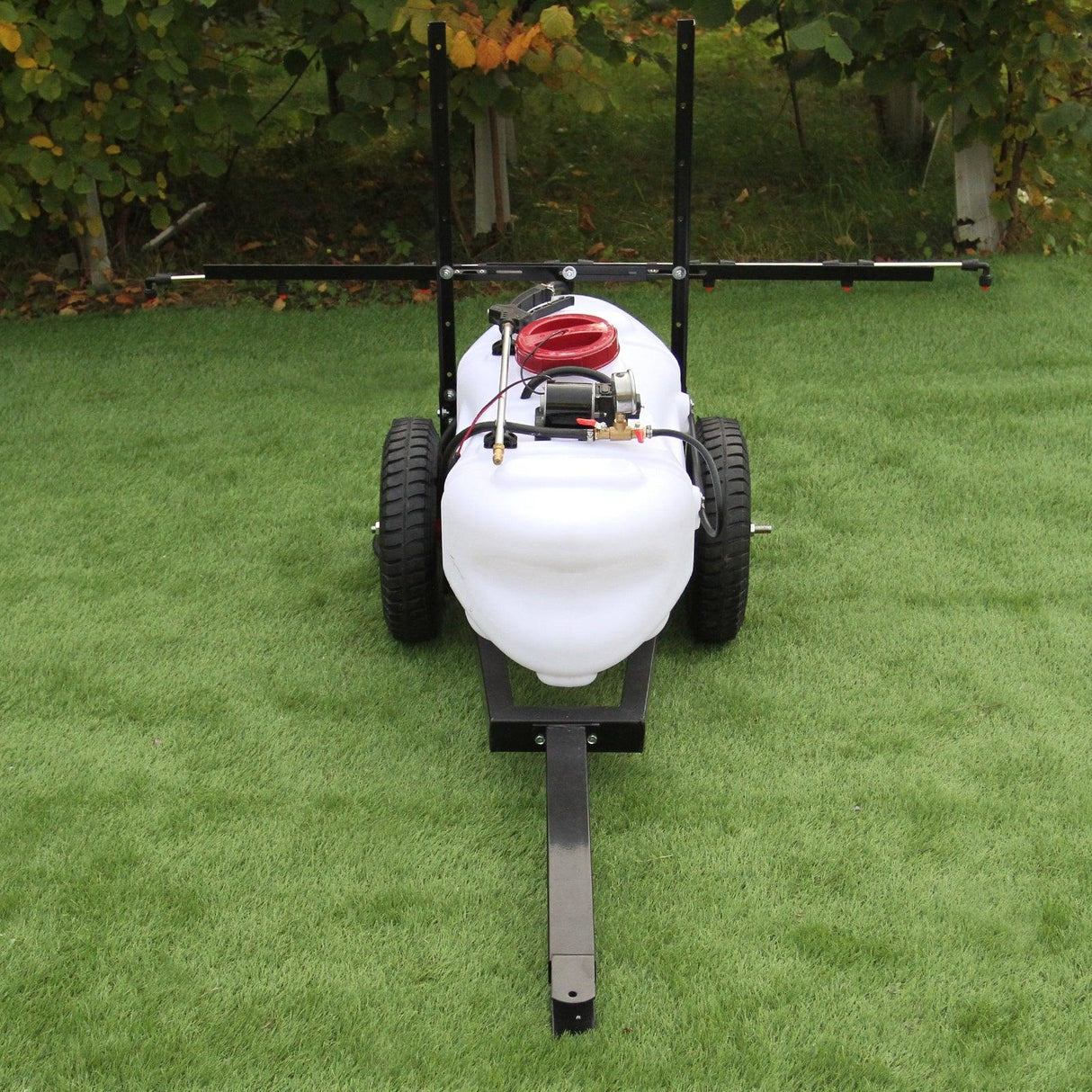100L ATV trailer and sprayer with a white tank, black wheels, and a red pump, set on green grass with trees in the background