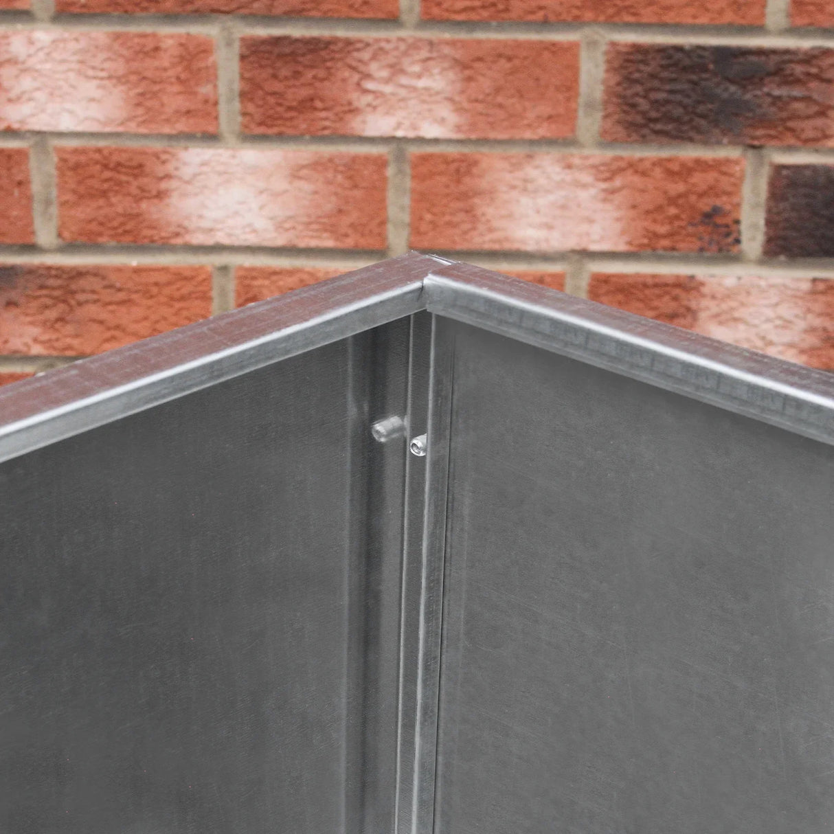 Galvanised feed store with three compartments, featuring a sturdy metal construction and smooth, shiny surface against a brick background