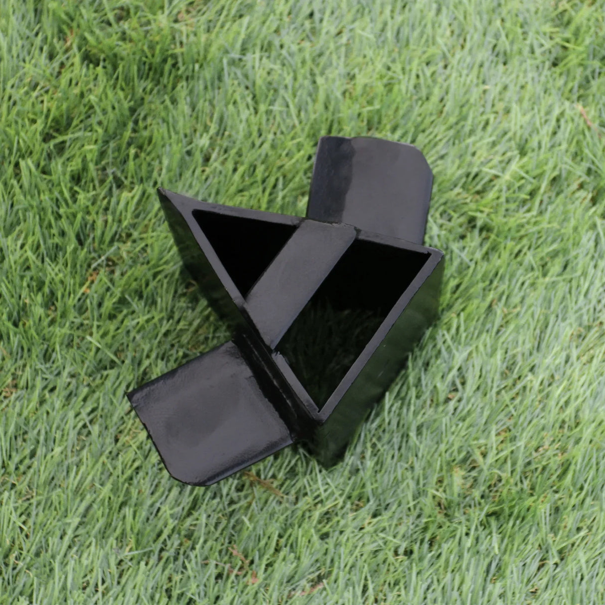Black metal log splitter attachment with triangular and rectangular openings, designed for T-Mech Log Splitter, resting on green grass