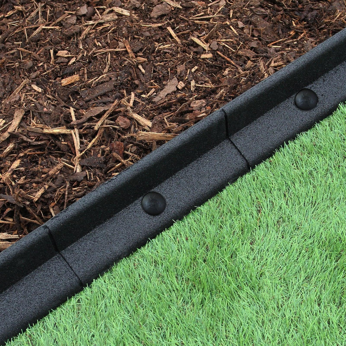 Flexible black lawn edging, 1.2m long, with smooth texture, neatly separating mulch from green grass for a tidy garden look