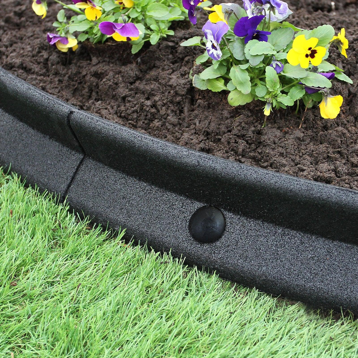 Flexible black lawn edging 1.2m x 6, featuring a smooth texture, curved shape, and surrounded by colorful flowers and lush green grass